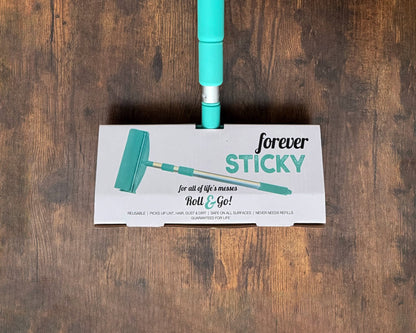 A floor mop head with a turquoise handle and a white printed label that reads 'forever STICKY Roll & Go!' placed on a dark wood floor.
