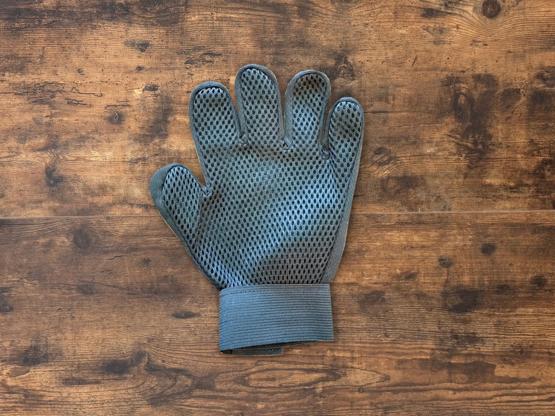 A single gray silicone-coated gardening glove with a breathable mesh palm, laid flat on a rustic wooden surface.