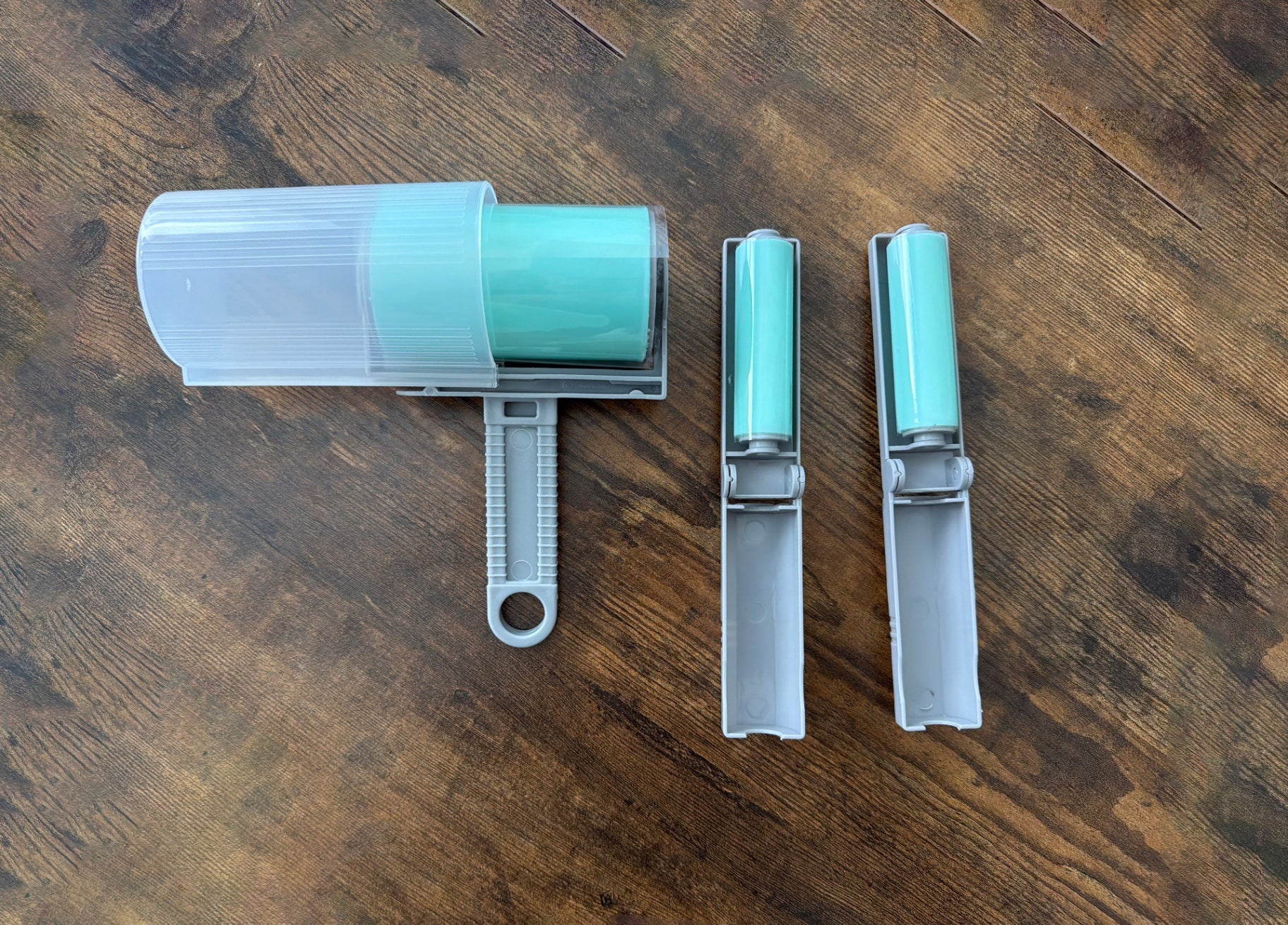 A lint roller set with three views: one showing the roller covered in mint green lint inside a clear case, and two side views showing the gray and mint green roller mechanism.