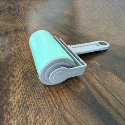 A mint green and gray lint roller with a textured gray handle, resting on a dark brown wooden tabletop.